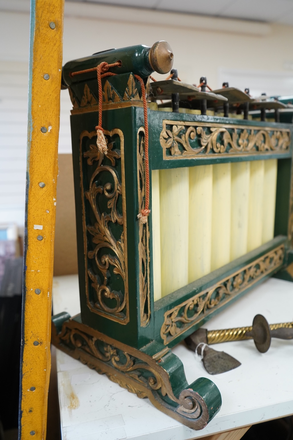 A green and gold painted wooden Javanese Gamelan Slenthem musical instrument, 61cm wide, 46cm high, together with two hammers